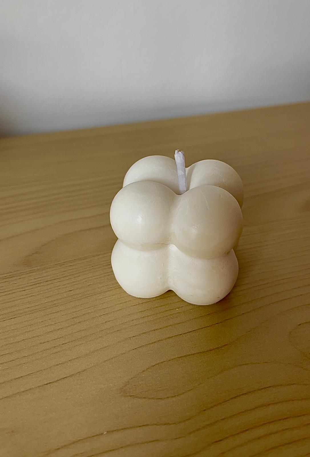 Vela mini en forma de cubo de burbujas en color crema, colocada sobre superficie de madera clara.