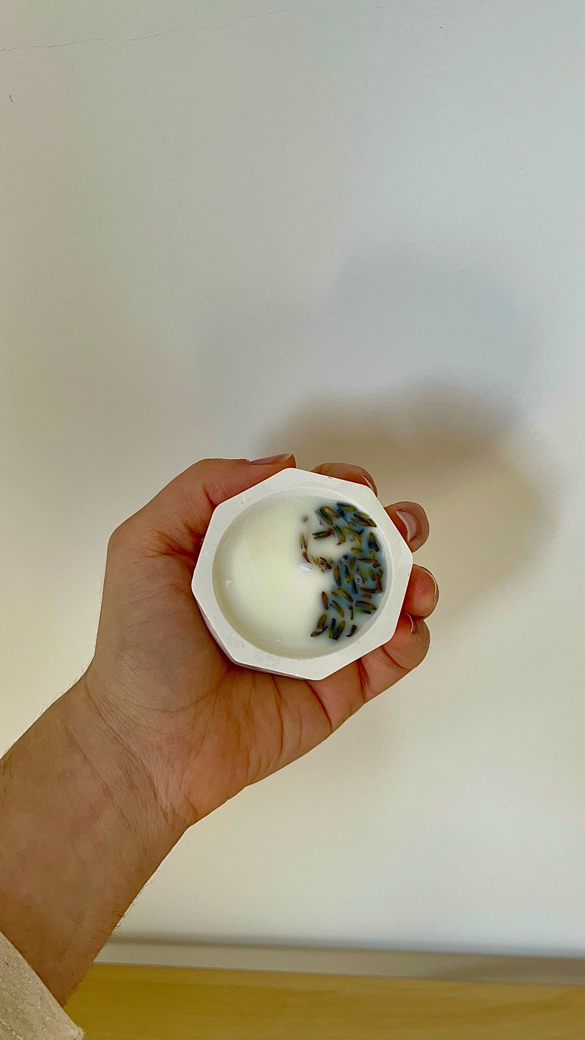 Vela artesanal de lavanda sostenida en la mano, con flores secas visibles en la superficie de la cera.