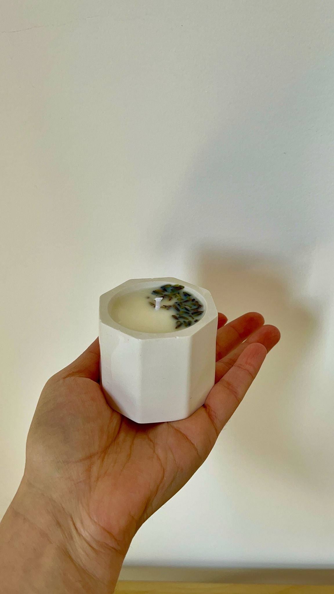 Vela de lavanda artesanal sostenida en la mano, destacando el contraste entre la cera blanca y las flores secas decorativas