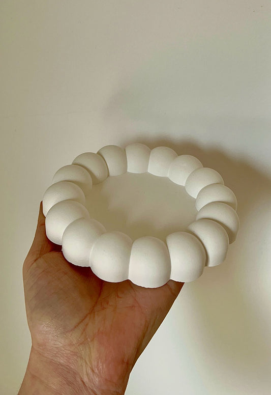 Bandeja redonda de burbujas 'A' sostenida en una mano, con diseño circular de esferas y acabado blanco mate