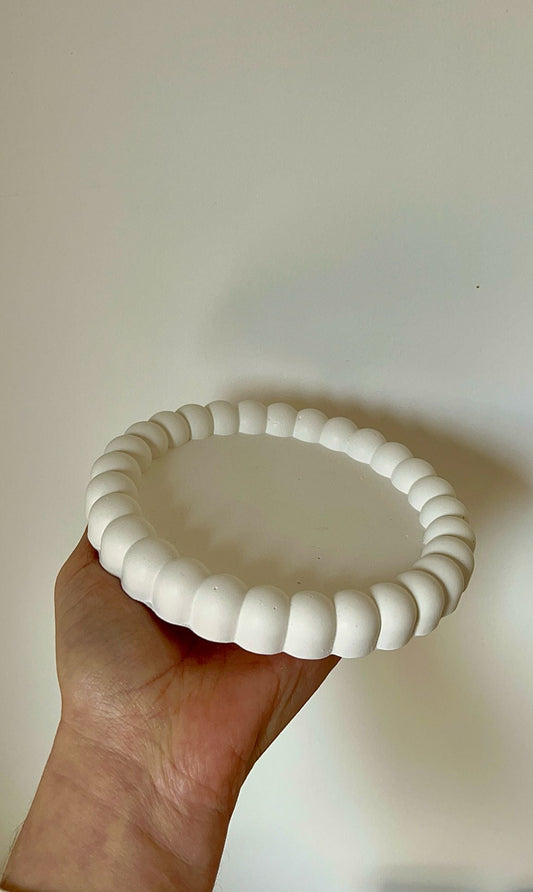 Bandeja decorativa redonda tipo burbujas sostenida en la mano, con acabado blanco mate y diseño texturizado