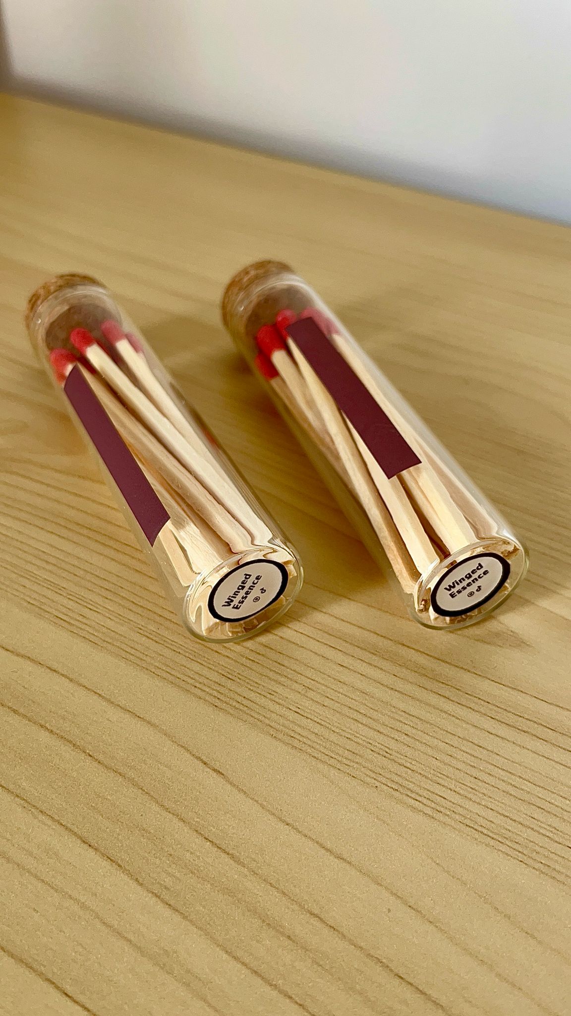Dos porta fósforos de vidrio con cabezas de fósforo rojas visibles y base de corcho, colocados sobre superficie de madera