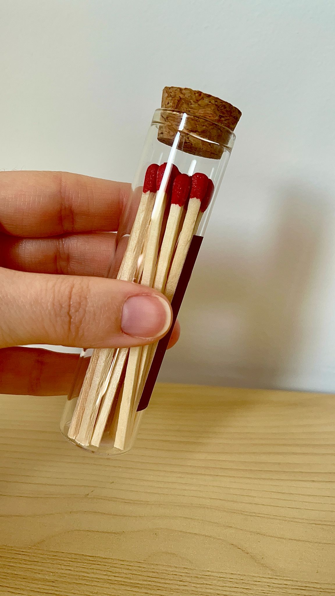 Mano sosteniendo un porta fósforos decorativo con fósforos rojos dentro de un tubo de cristal cerrado con corcho.