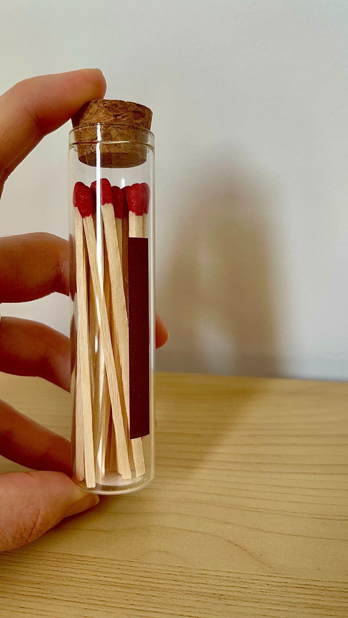 Porta fósforos de cristal sostenido en la mano, mostrando los fósforos rojos y el diseño del frasco.