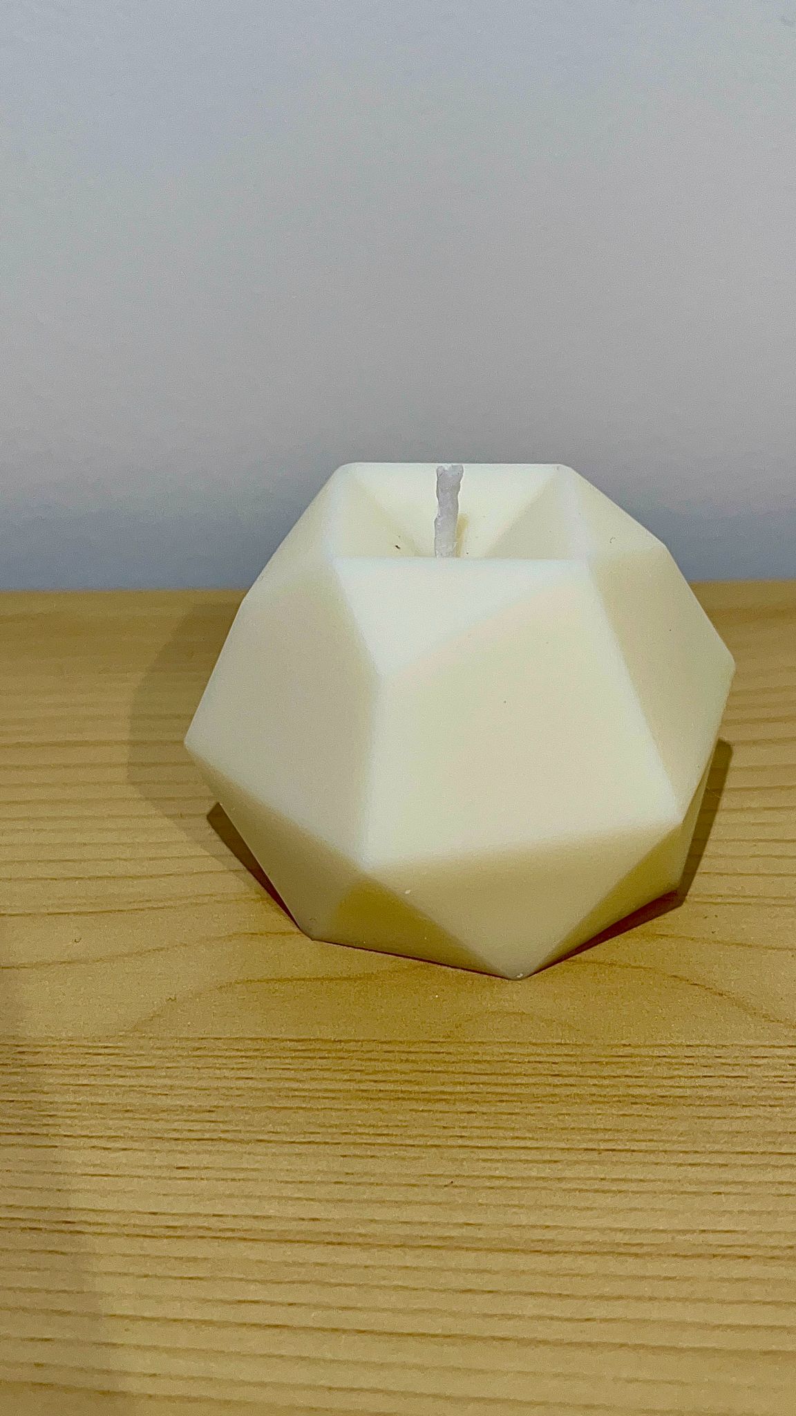 Vela decorativa con forma poliédrica en color crema, colocada sobre superficie de madera, con diseño geométrico facetado