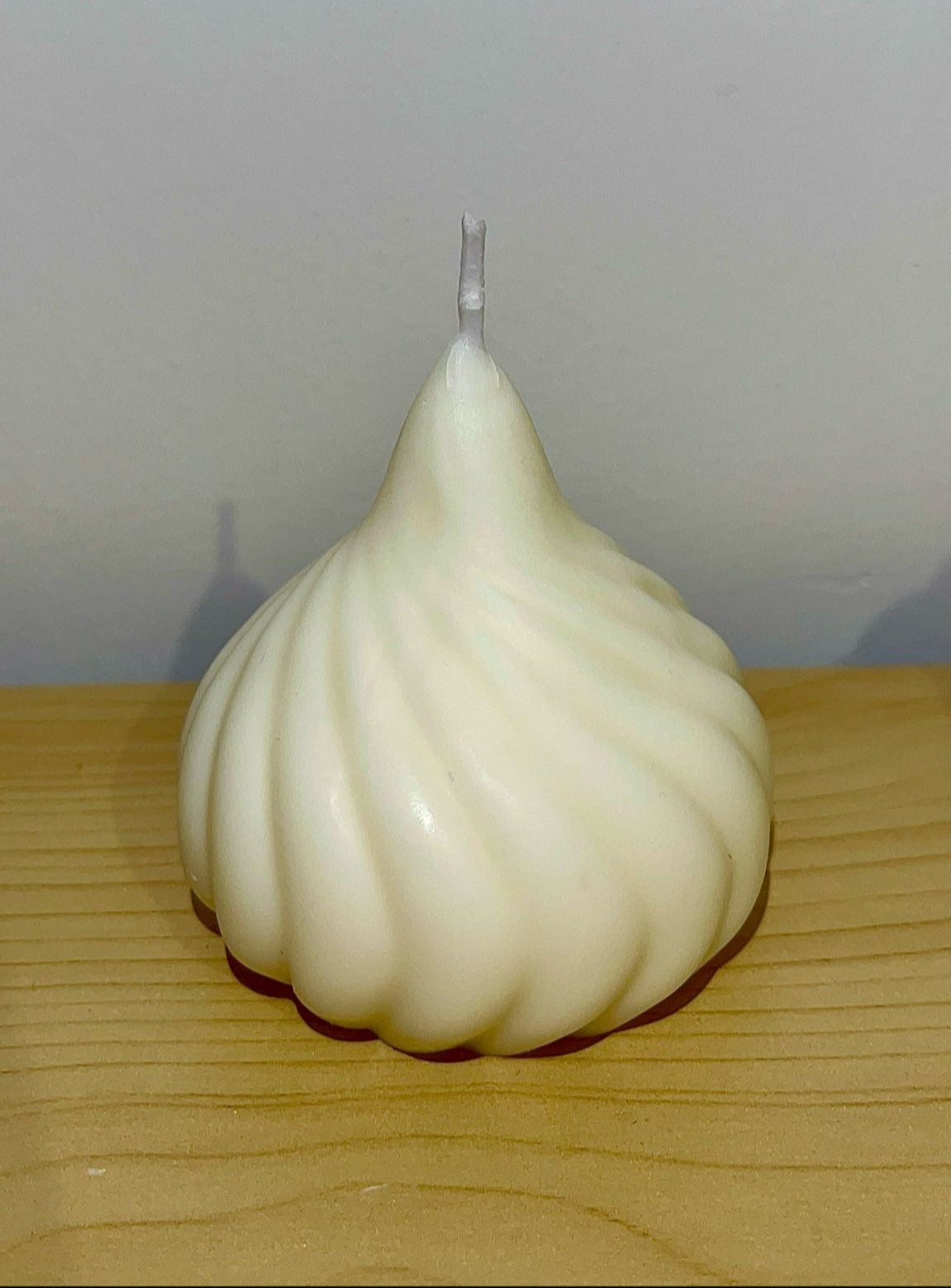 Vela decorativa en forma de espiral con acabado perlado en tono crema, colocada sobre superficie de madera
