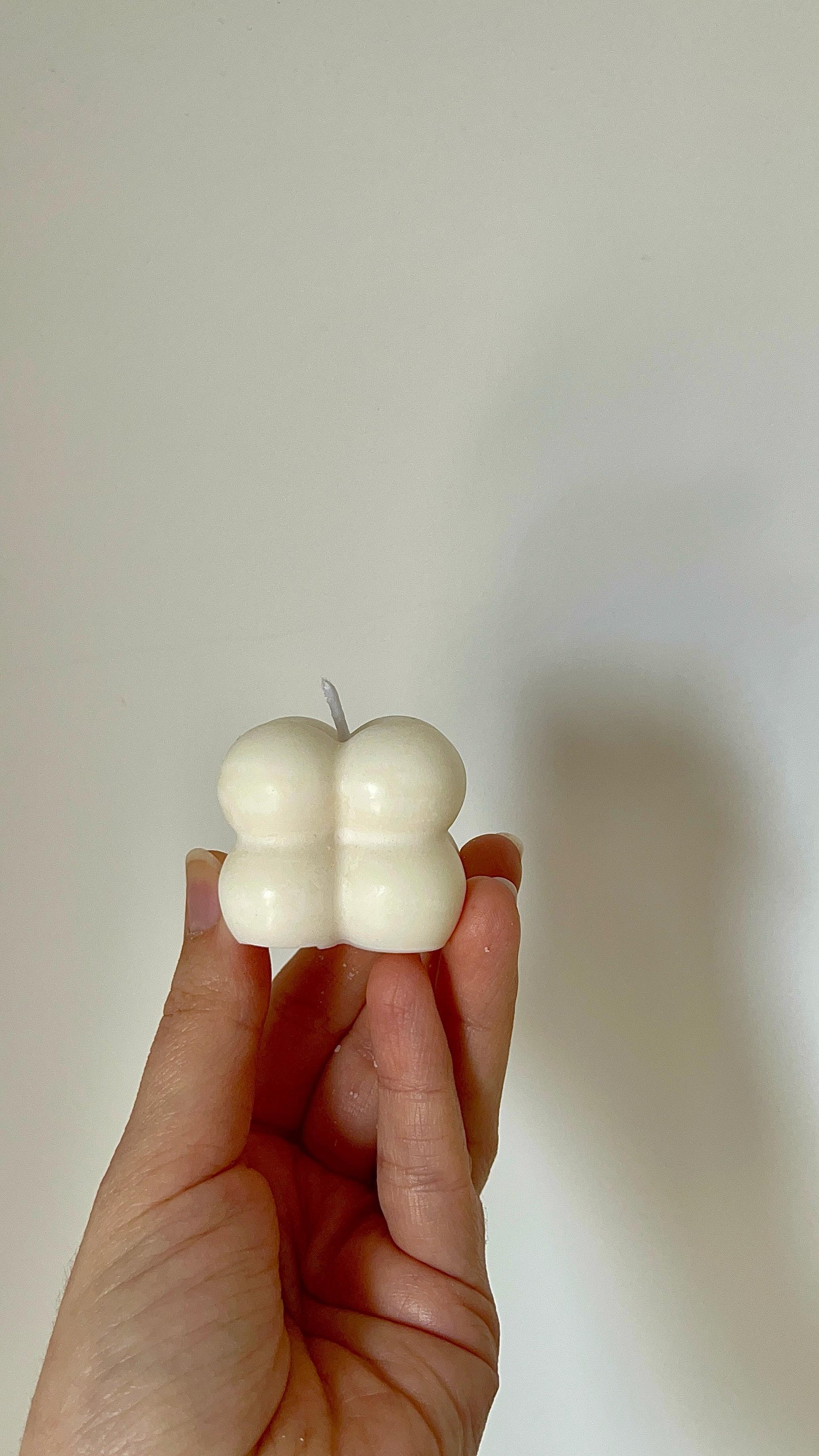 Vela decorativa mini en forma de cubo de burbujas, sostenida de frente en posición vertical