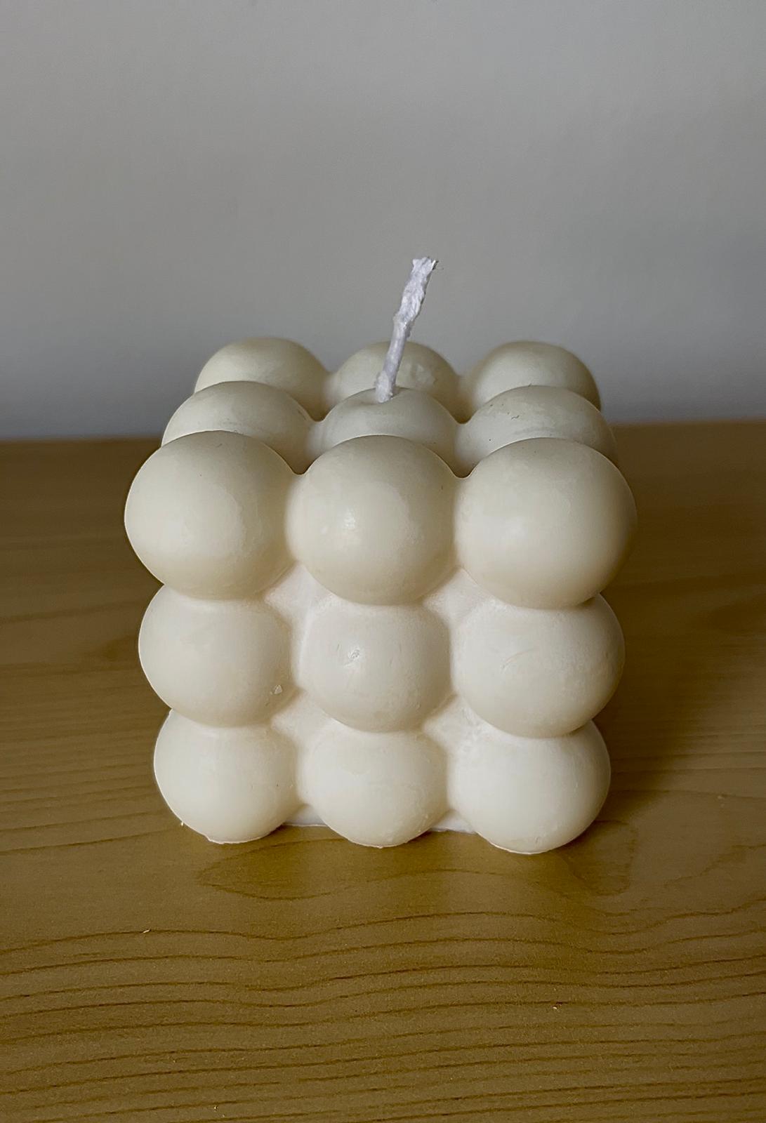 Vela maxi en forma de cubo de burbujas color crema, colocada sobre superficie de madera clara