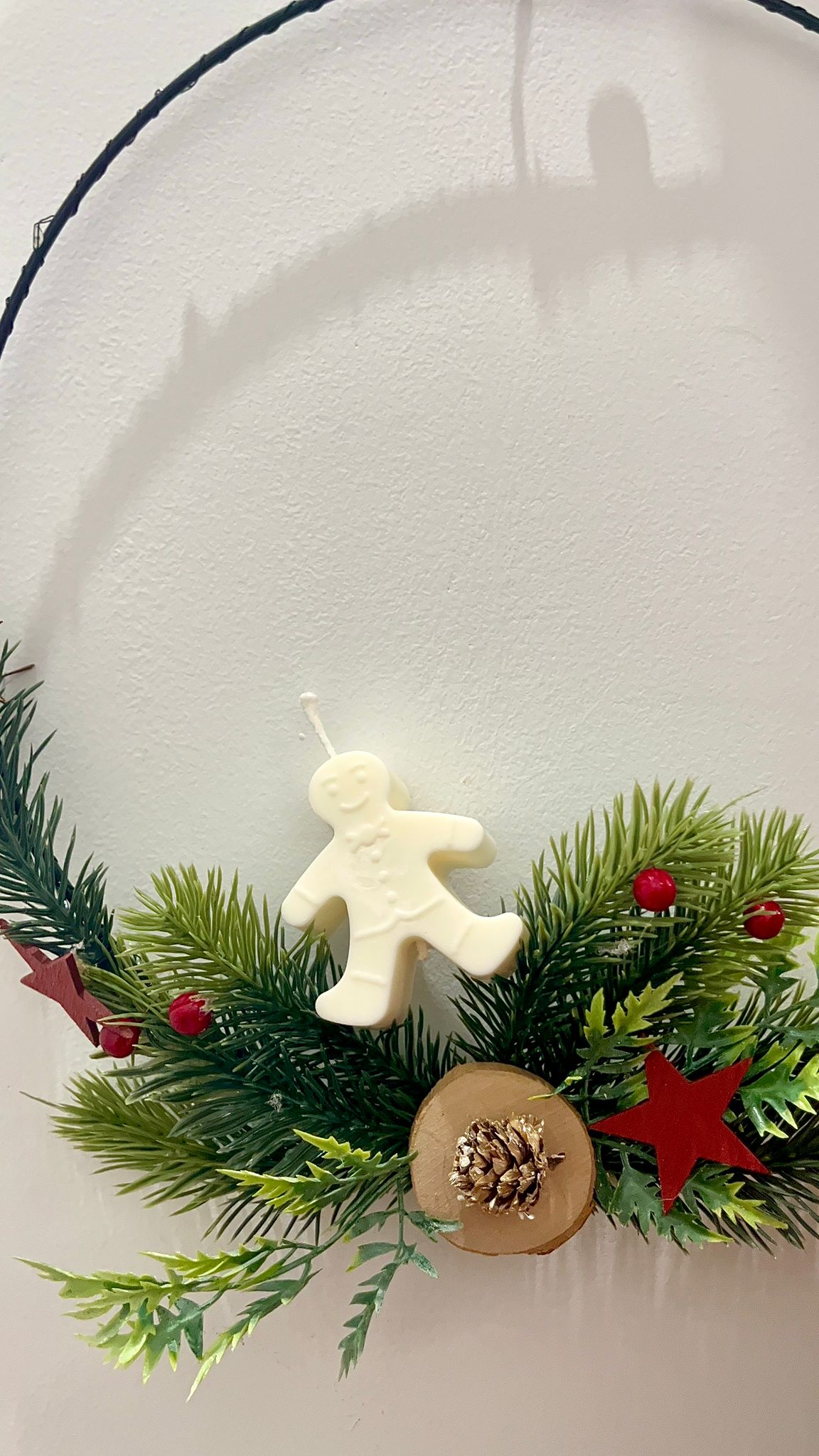 Vela decorativa Galleta de Invierno de Winged Essence en forma de muñeco de jengibre, hecha con cera de soja vegetal, sobre corona navideña con ramas y piñas.