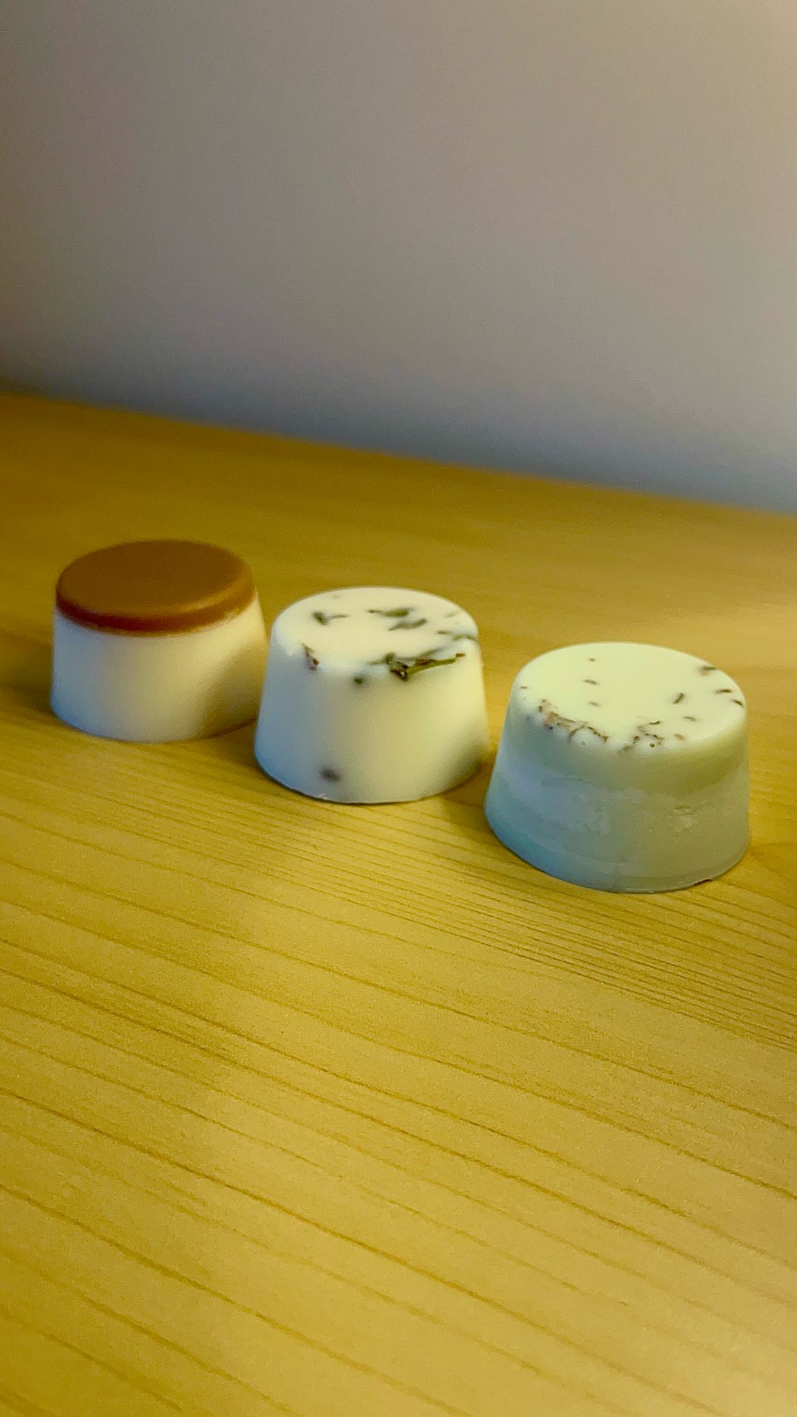 Trío de melts aromáticos de cera de soja sobre superficie de madera: uno con parte superior marrón, otro con flores secas de lavanda, y el tercero completamente blanco con textura botánica