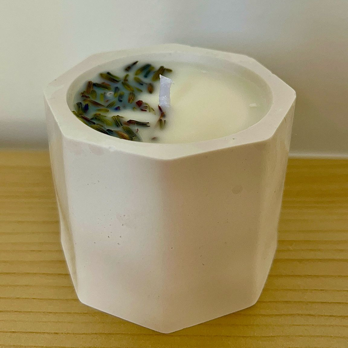 Vela de lavanda en recipiente blanco, colocada sobre superficie, con decoración de flores secas en un lateral, en el dormitorio para ayudar a dormir y relajarse
